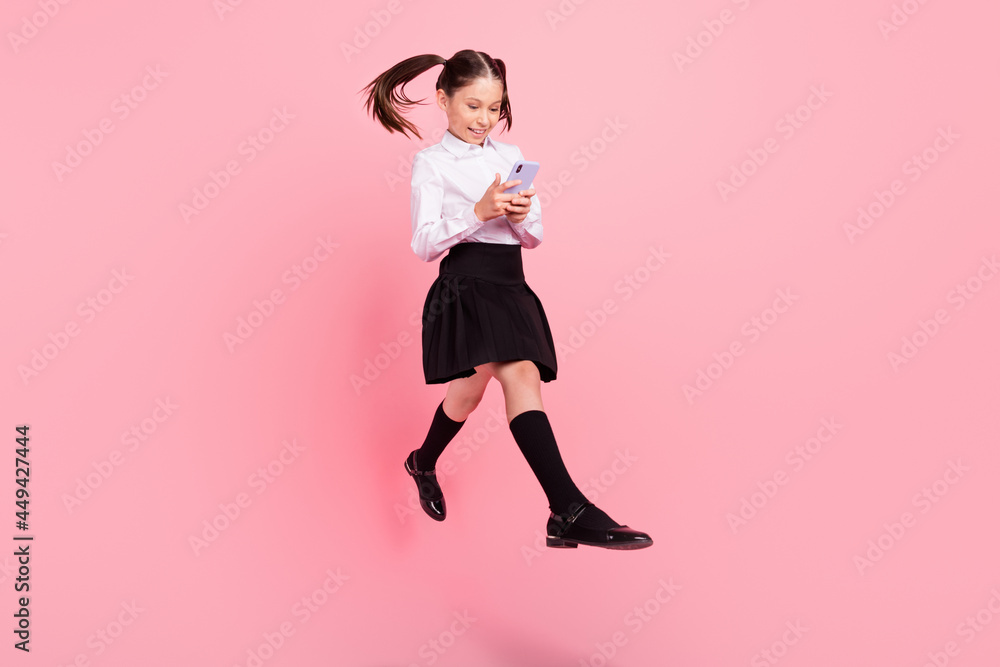 Full size photo of young little brunette tails haired girl jump hold phone walk wear formalwear uniform isolated on pink color background Full size photo of young little brunette tails haired girl jump hold phone walk wear formalwear uniform isolated on pink color background