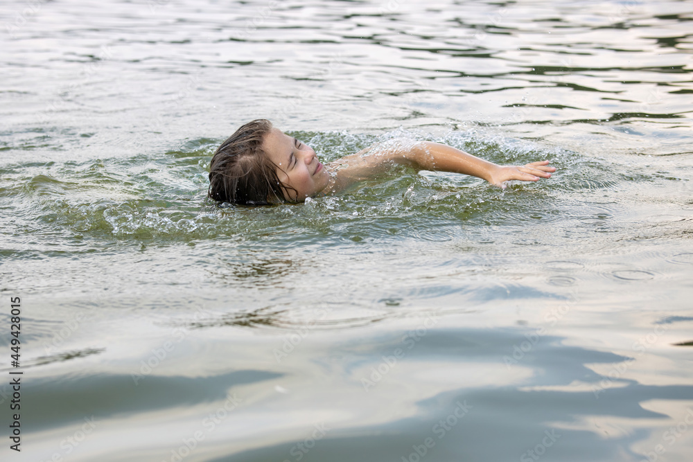 A teenage girl enjoys breaststroke swimming in the calm warm lake water.