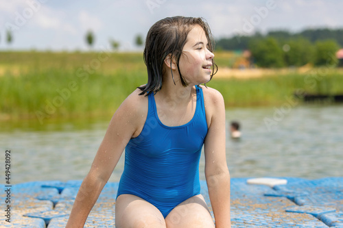 A teenage girl in a blue swimsuit sits on the pier and enjoys the beautiful summer weather