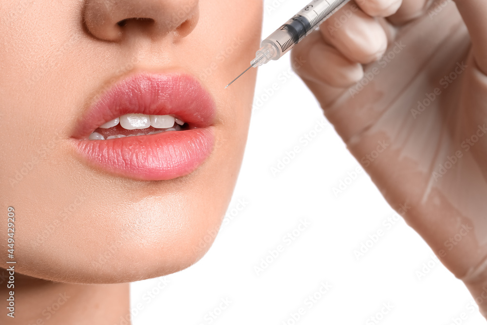 Young woman receiving filler injection in lips against white background, closeup