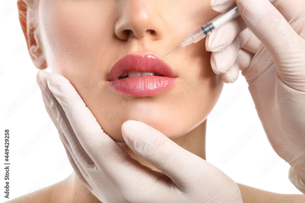 Obraz premium Young woman receiving filler injection in lips against white background, closeup