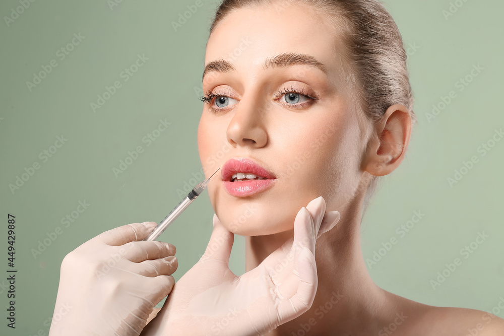 Fototapeta premium Young woman receiving filler injection in lips against color background