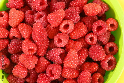 Ripe raspberry in a green plate on yellow background.