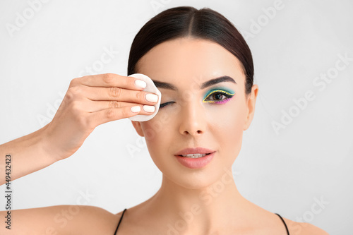 Beautiful young woman removing makeup on light background