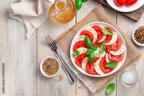 Italian caprese salad with sliced tomatoes, mozzarella cheese, olive oil and basil on a beige wooden background.
