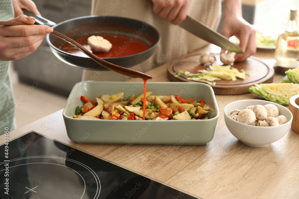 Woman pouring sauce onto baked potatoes in kitchen Woman pouring sauce onto baked potatoes in kitchen