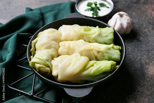 Frying pan with uncooked cabbage rolls and sour cream on grunge background