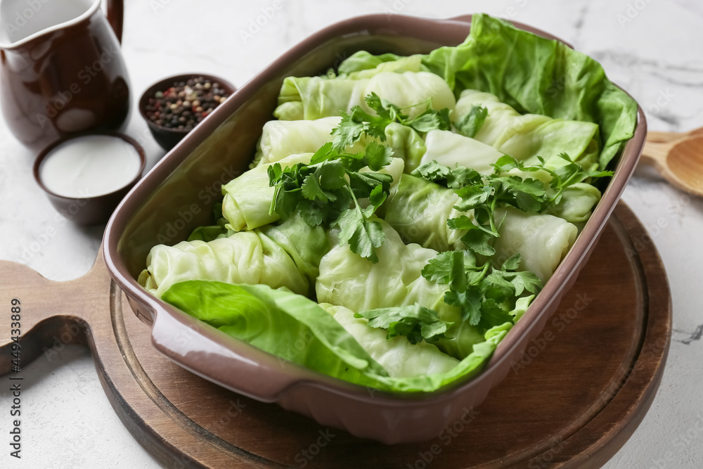 Baking dish with uncooked cabbage rolls and parsley on light background Baking dish with uncooked cabbage rolls and parsley on light background