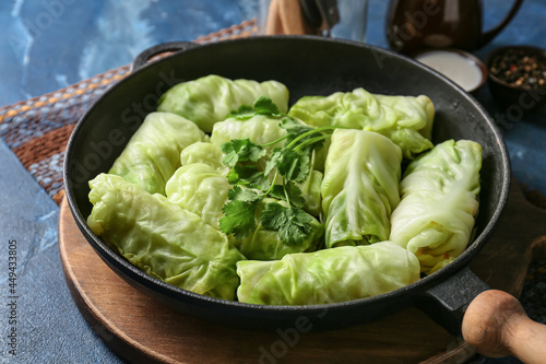 Frying pan with uncooked cabbage rolls on color background