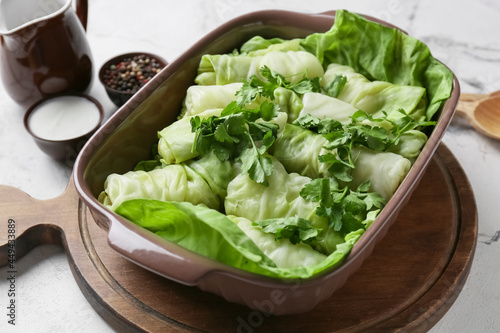 Baking dish with uncooked cabbage rolls and parsley on light background