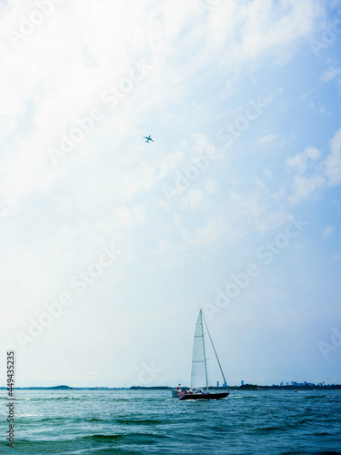 Seascape with an airplane in the white sky and a yacht sailing on the turquoise-colored ocean water