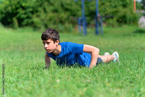 teenage boy exercising outdoors, sports ground in the yard, he does push-ups on the green grass field, healthy lifestyle