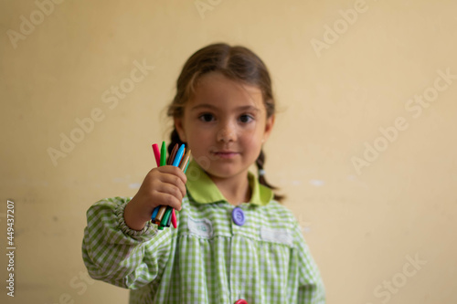 Adorable niña en su primer día de colegio  vestida con mandilón a cuadros verdes dibujando y mirando libros.