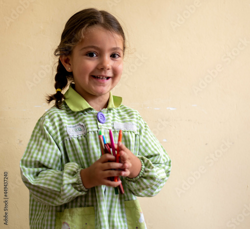 Adorable niña en su primer día de colegio  vestida con mandilón a cuadros verdes dibujando y mirando libros.
