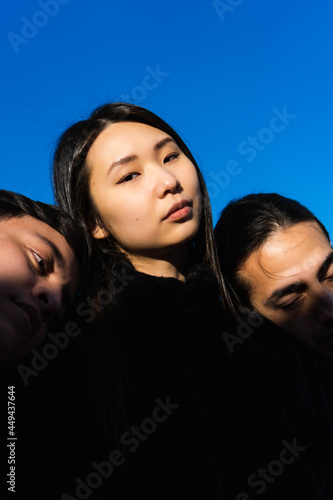 vertical photo of multiracial asian american woman with two latin men, blue sky background, daylight in the morning. three people, polyamory photo