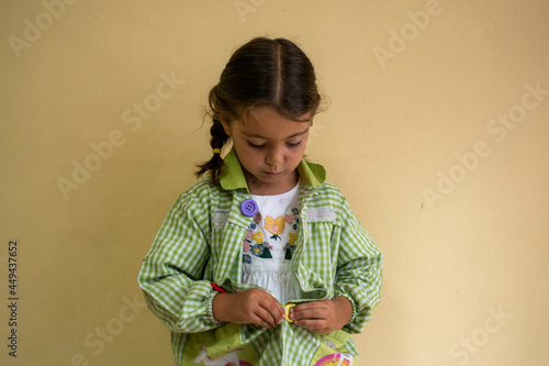 Adorable niña en su primer día de colegio  vestida con mandilón a cuadros verdes dibujando y mirando libros.