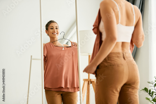 Cuadro en lienzo Young happy woman chooses clothing and looking herself in mirror at home