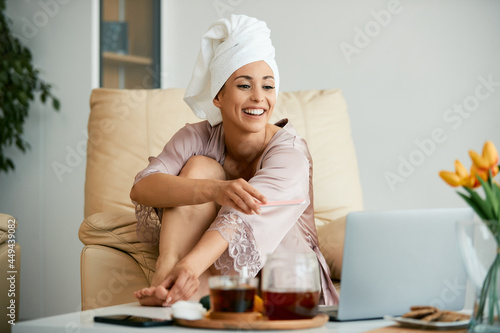 Fotografia Happy beautiful woman uses laptop while having pedicure at home.