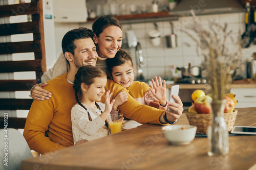 Cheerful family use smart phone and wave during video call from home. © Drazen