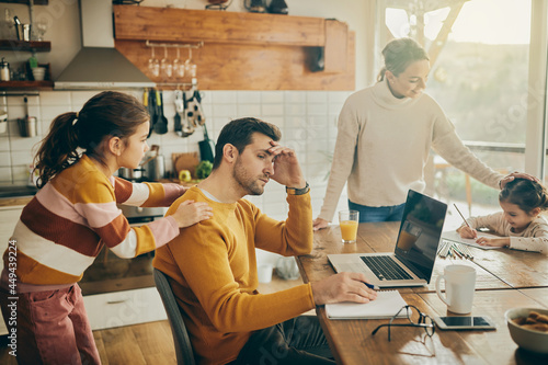 Exhausted father works on laptop while being with his family at home. photo