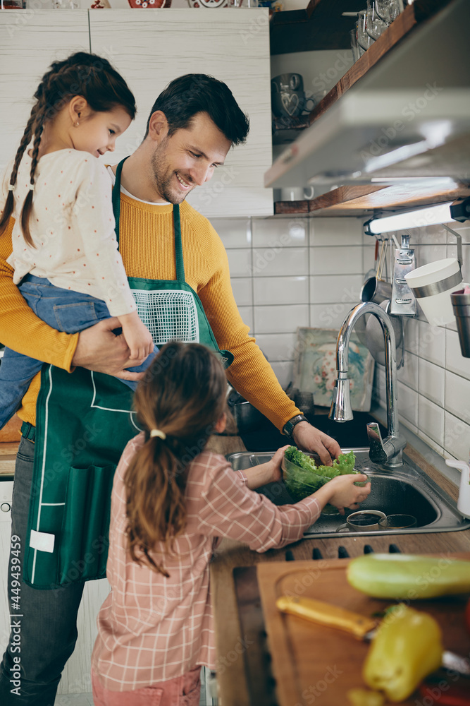 © Drazen - Happy father and daughters wash lettuce while preparing salad in the kitchen.