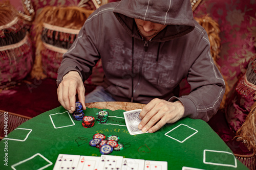 A suspicious man with a hood on the face plays a poker card in an expensive casino interior