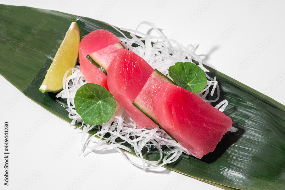 Tuna sashimi on white background. Traditional Japanese food. Raw yellow fin tuna fish served with decor, cucumber, daikon and lime on bamboo leaf. Sushi restaurant menu. Copy space, close up