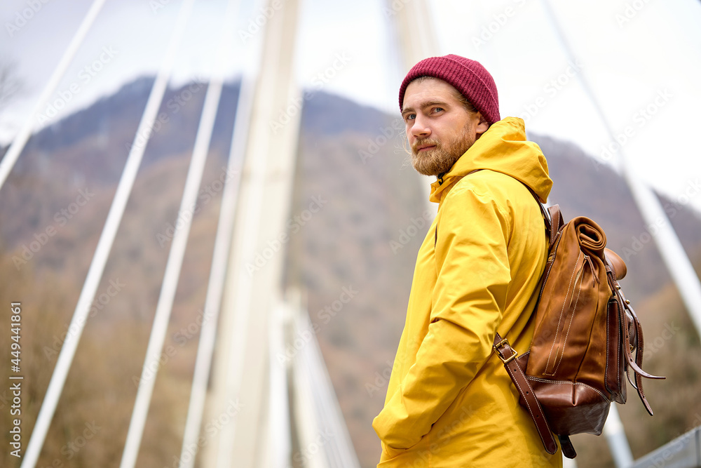 Man in yellow coat walking alone on pedestrian pathway on bridge in an urban park. Healthy lifestyle, travel, adventure, hiking concept