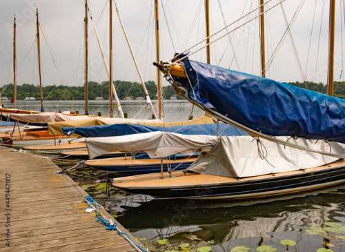 Wroxham, Norfolk Broads, UK – July 2021. Sailing boats moored along the wooden staging on the side of Wroxham Broad during the annual sailing regatta open week.