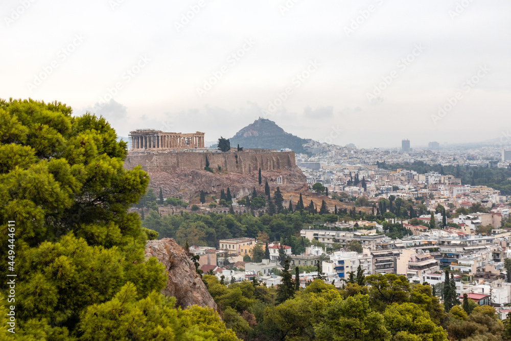 Acropolis (Parthenon, Temples), Mount Lycabettus and white city buildings with vivid pine greenery. Athens ancient landmark from Filopappou Hill on cloudy day Acropolis (Parthenon, Temples), Mount Lycabettus and white city buildings with vivid pine greenery. Athens ancient landmark from Filopappou Hill on cloudy day