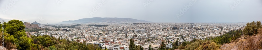 Wide panorama on Athens city center with white architecture buildings, Acropolis and mountains in vivid greenery on cloudy dramatic day from Filopappou Hill