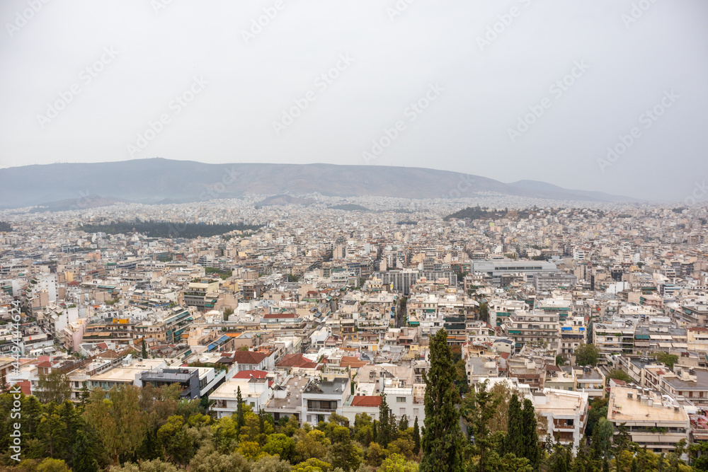 Athens city center streets with white architecture, mountain silhouette and greenery on gray foggy day. Rooftop view from Filopappou Hill park near Acropolis, Greece