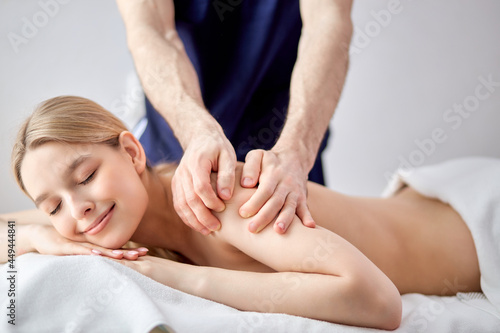 Cropped Confident Nice Male Masseur Therapist In Cosmetology Room Doing Massage To Female On Back, Shirtless Lady Lying On Bed Enjoying Spa Treatment By Professional, Closing Eyes. Side View Portrait