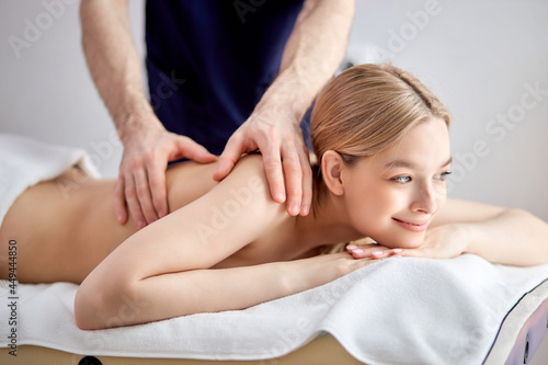 Close-up portrait of adorable caucasian female lying on couch getting massage, looking at side in contemplation, smiling cutely. shirtless woman lying on belly