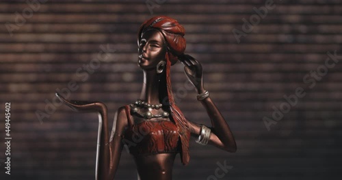 A beautiful statuette of an oriental girl stands on a brown background. This is an old toy of a woman in beads and with long thin hands. A statuette of a woman in a headdress.