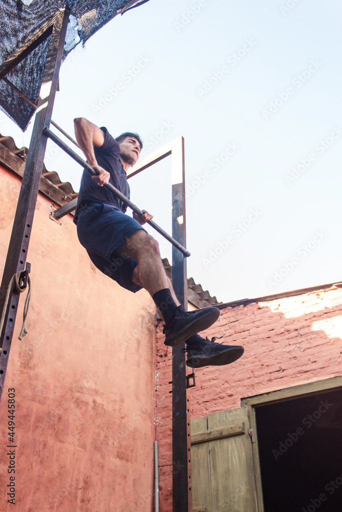 Young athletic man climbing on the metal bar. Cross fit training.