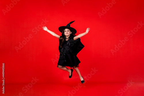 a little girl in a witch costume jumps on a red background with a copy of the space