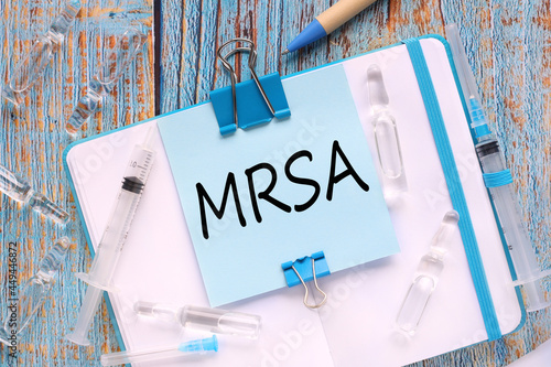 MRSA Methicillin-resistant Staphylococcus Aureus. the sticker is attached to the notebook with a clerical clip. notebook on a wooden table in blue photo