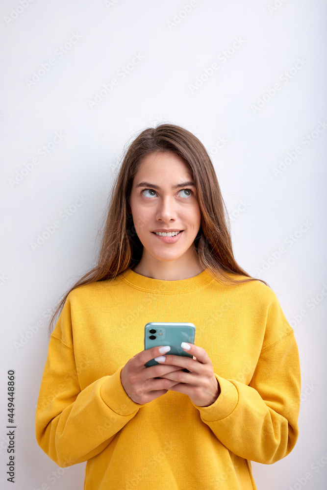 adult woman thinking while chatting with boyfriend, flirting, typing message, isolated on white studio background, copy space for advertisement. Young lady in yellow casual wear looks up, biting lips adult woman thinking while chatting with boyfriend, flirting, typing message, isolated on white studio background, copy space for advertisement. Young lady in yellow casual wear looks up, biting lips