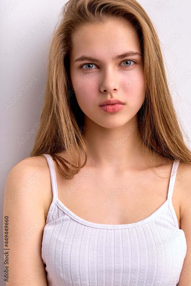 Awesome caucasian female with natural long brown hair posing at camera, in white casual undershirt, teenage girl is looking confident, young cute model 16 years old. copy space. portrait Awesome caucasian female with natural long brown hair posing at camera, in white casual undershirt, teenage girl is looking confident, young cute model 16 years old. copy space. portrait