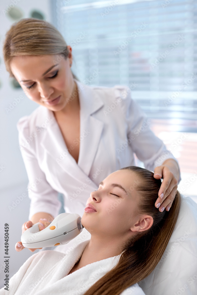 woman lying in spa salon getting massage for face with professional apparat, lovely caucasian woman in beauty and spa concept. copy space. young professional beautician applying device on face