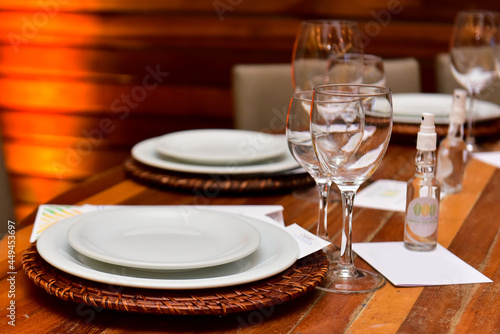 table set for dinner with white plates, glass glasses and alcohol to sanitize hands 