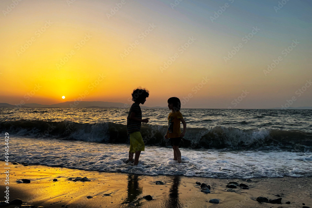 Two happy kids playing in the sea at sunset