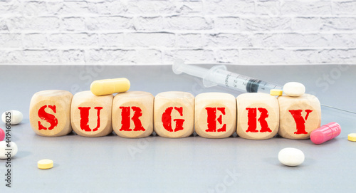 The word SURGERY is written on wooden cubes near a stethoscope on a wooden background. Medical concept