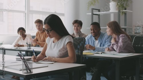 Upset asian teenage girl nerd suffering from bullying, groupmates laughing and throwing papers balls at her