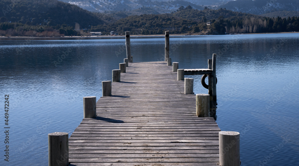 Naklejka premium The wooden docks into the placid lake. View of the blue sky, forest and mountains reflection in the water. 