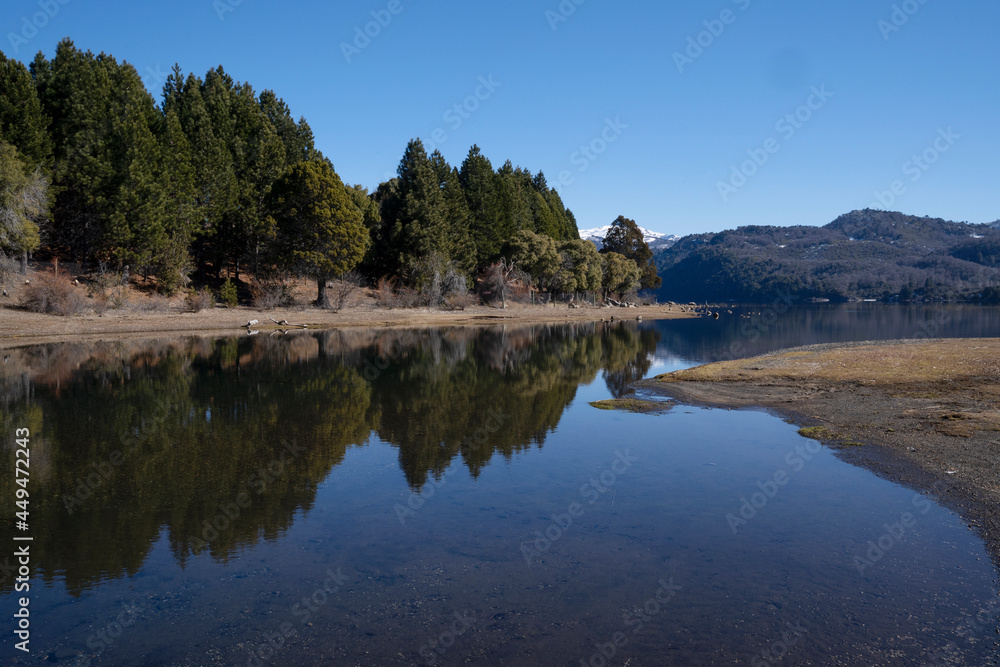The perfect reflection of the blue sky, green forest and mountains in the lake's water surface. 