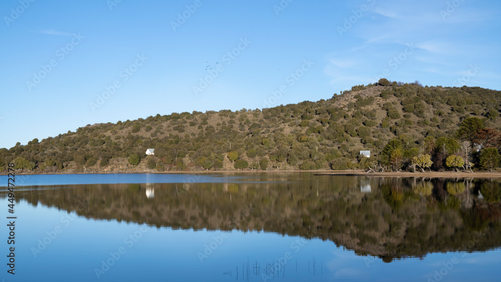 Symmetry in nature. Panorama view of the calm lake. The hills, green forest and clear blue sky reflection in the water surface. Symmetry in nature. Panorama view of the calm lake. The hills, green forest and clear blue sky reflection in the water surface.