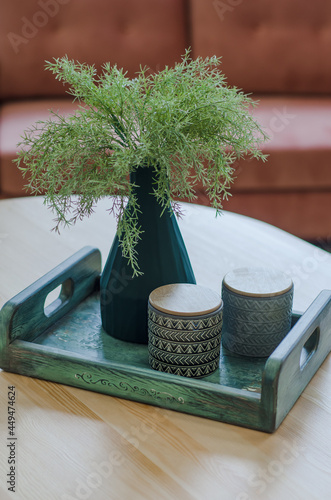 Still life in  apartment in green tones on  pink background. Decorative interior composition of green branches, clay vessels and  wooden tray.