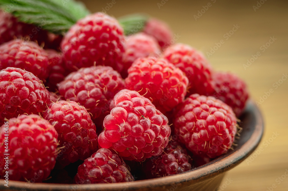 Bowl with fresh ripe delicious raspberries and a green leaf on a wooden background. Closeup Bowl with fresh ripe delicious raspberries and a green leaf on a wooden background. Closeup